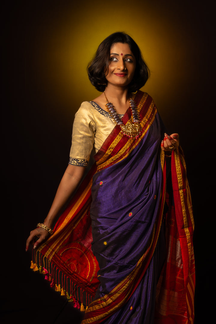 A women is dressed up and is posing by wearing beautiful purple saree with matching jewelry.