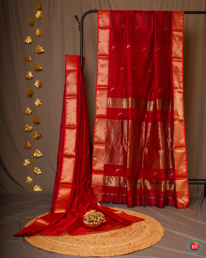 Elegant red Maheswari handloom silk cotton parrot saree Devika is pleated and displayed on a stand.